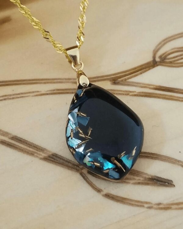 Collier artisanal mystérieux et élégant en nacre bleue et éclat de laiton sur fond noir.