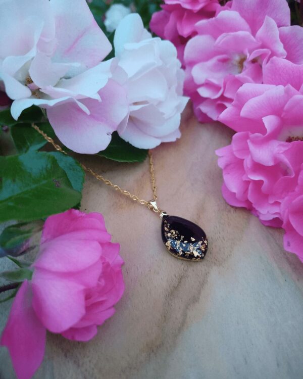 Un collier lumineux et élégant, sur fond noir profond, parsemé de feuilles d'or, soigneusement incrustées à la main.