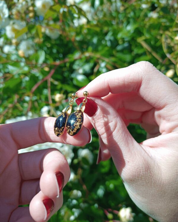 Boucles d'oreilles doré sur fond noir, insertion de feuilles d'or, style raffiné et élégant. Bijoux pour femmes.