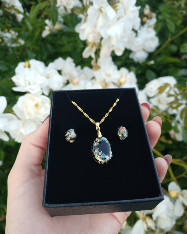 Parure de création artisanale faite en nacre colorée et feuilles d'or sur fond noir.